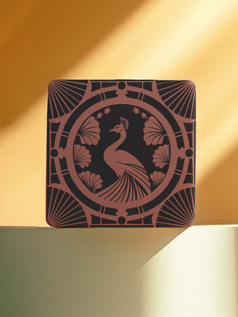 Square ceramic coaster featuring a detailed Art Deco peacock design in copper tones, surrounded by shell motifs and geometric fan patterns on a dark charcoal background, with protective cork base.